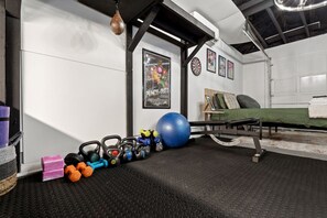 A gym with exercise equipment, a punching bag, and a bed with a green cover. - Marvin`s Gardens: Fenced Yard, Game Room, Pets! (Irondale)