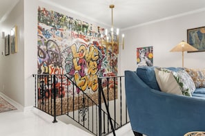 A living room with a blue sofa, a staircase with a graffiti mural, and a chandelier.