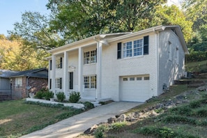 A two-story white brick house with a front porch, a garage, and a driveway leading to the entrance.