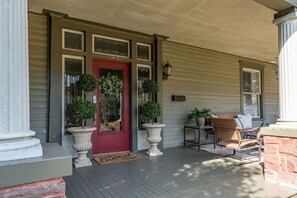 A porch with a red door, potted plants, and outdoor furniture.