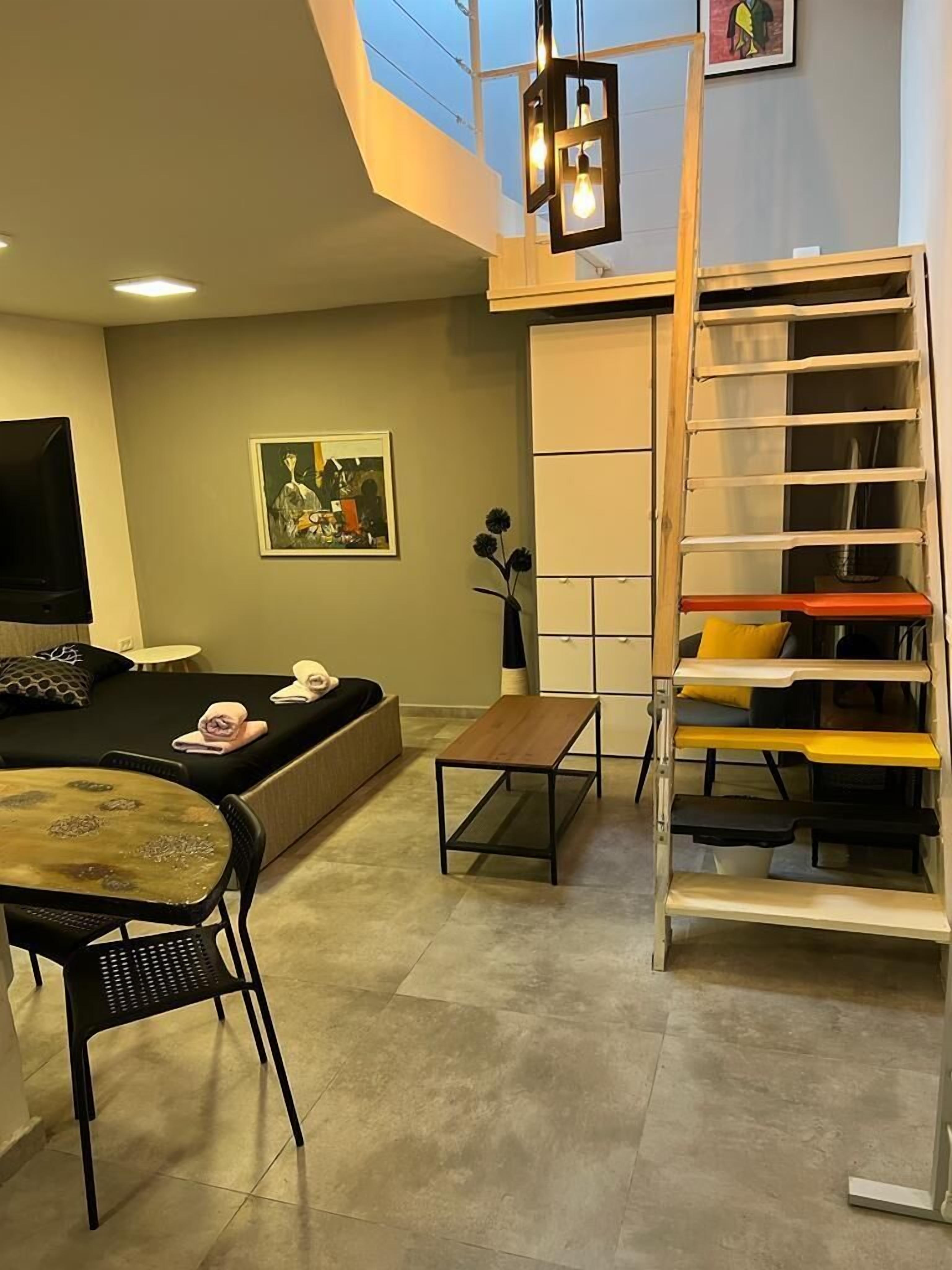 A modern living room with a sofa, a coffee table, a TV, a painting, and a staircase with storage shelves.