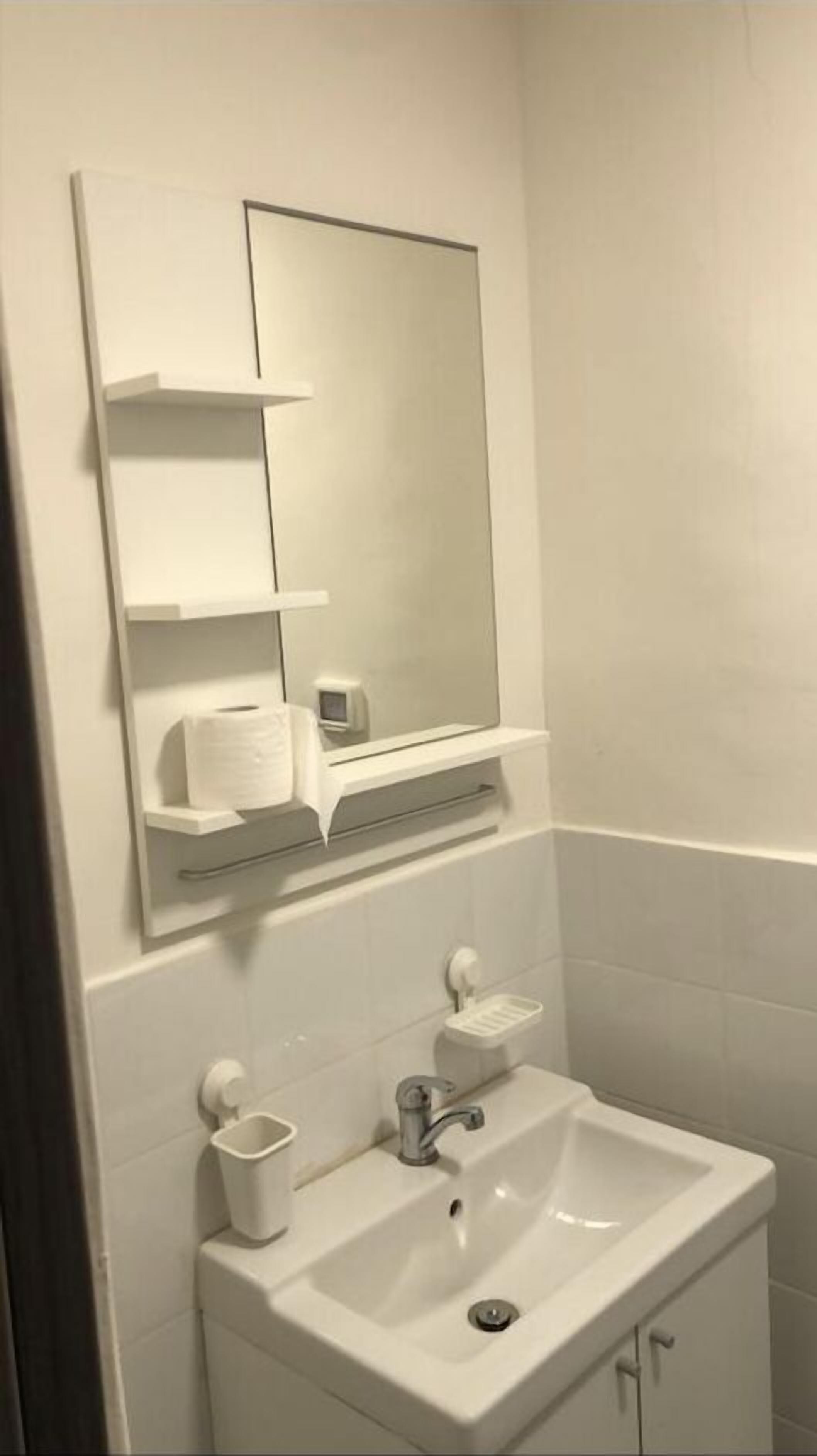 Un bagno con un lavandino bianco, uno specchio, un dispenser di sapone e una piccola mensola con un portaserviti.