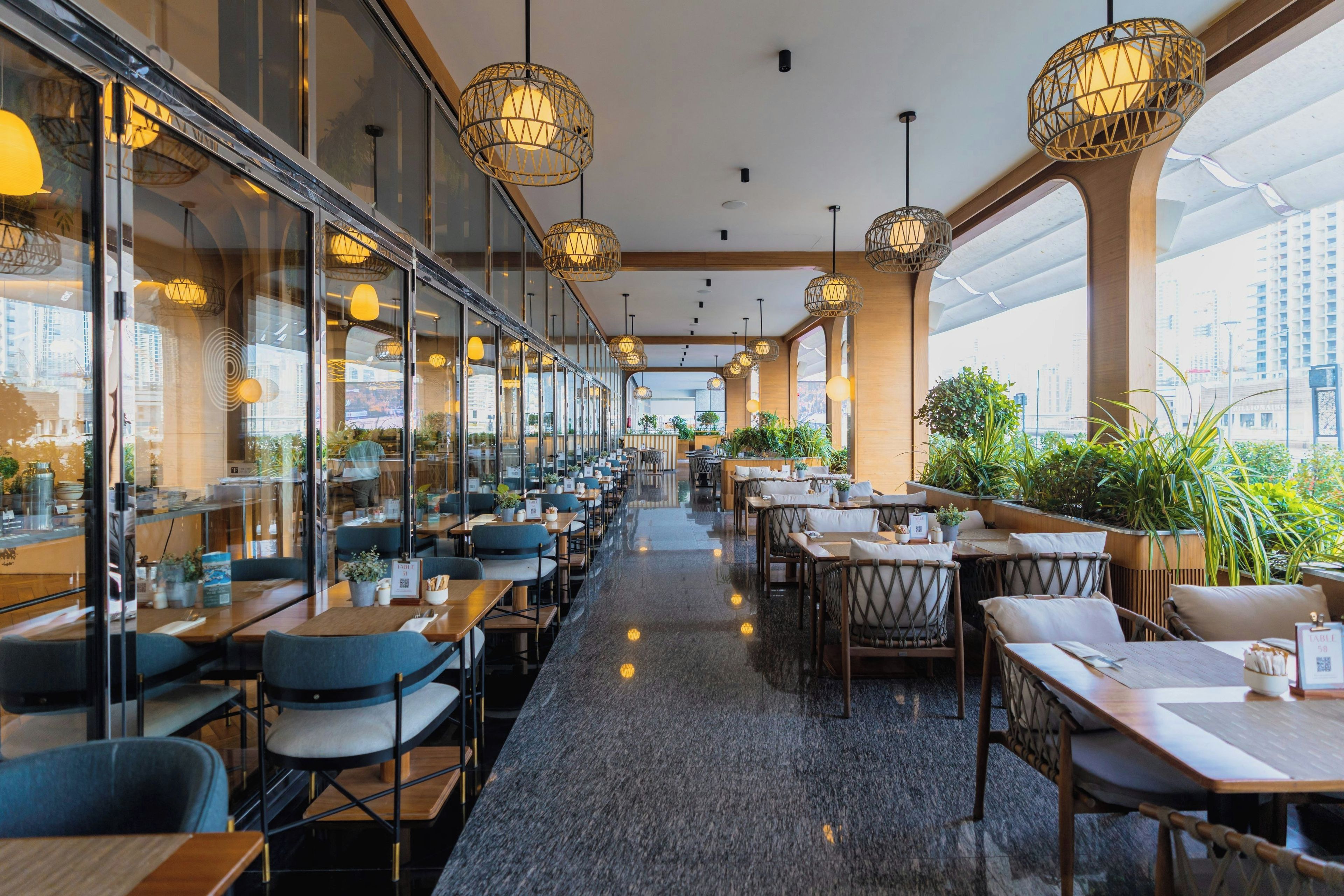 A modern restaurant with a long counter, multiple seating areas, and large windows offering city views.