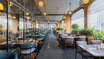A modern restaurant with a long counter, multiple seating areas, and large windows offering city views.