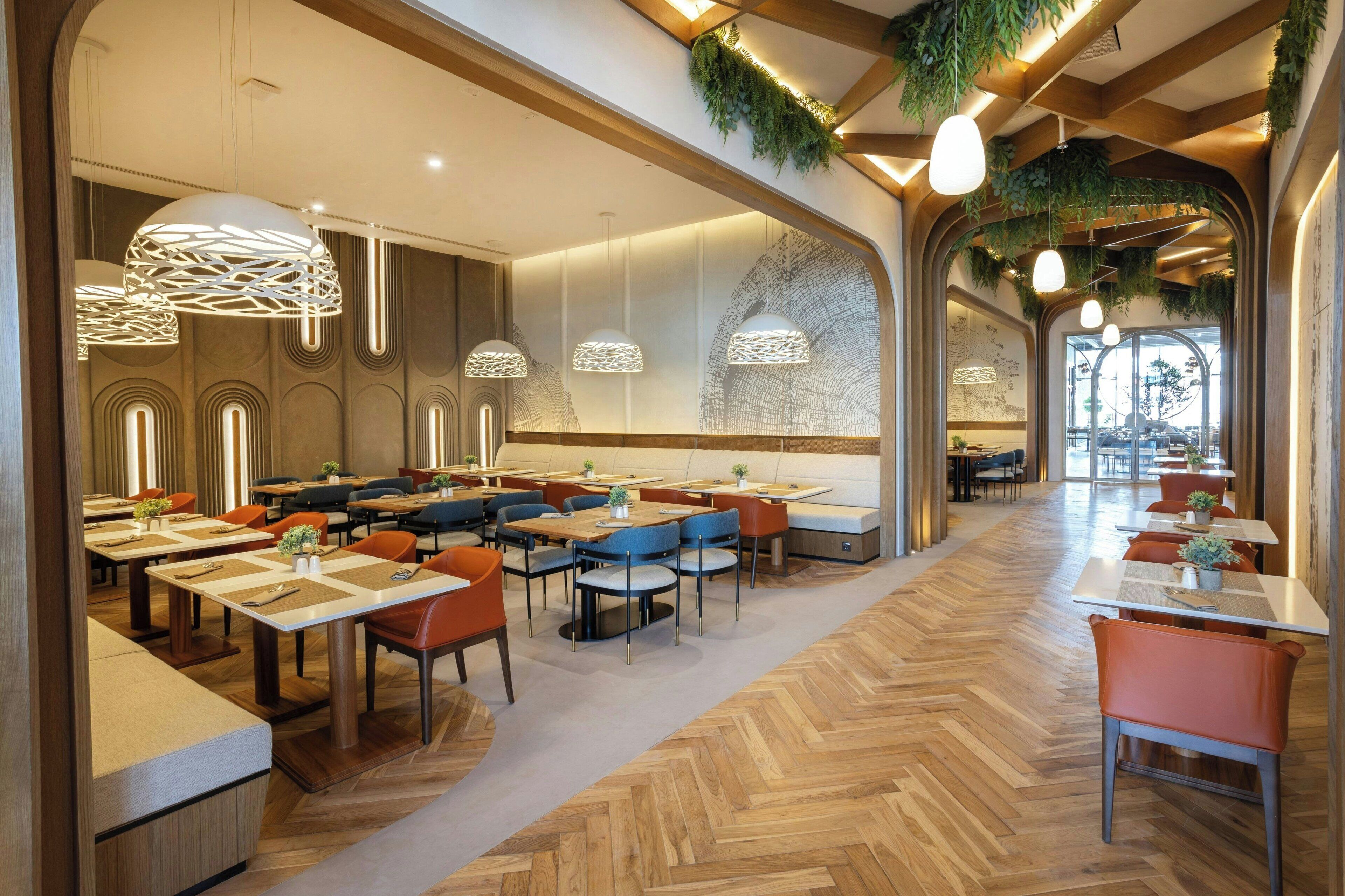 A spacious dining area with multiple tables and chairs, wooden flooring, and hanging pendant lights.