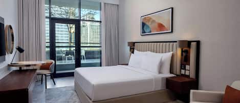Une chambre d’hôtel moderne dotée d’un grand lit, d’un bureau, d’une chaise et offrant une vue sur la ville grâce à de grandes fenêtres.
