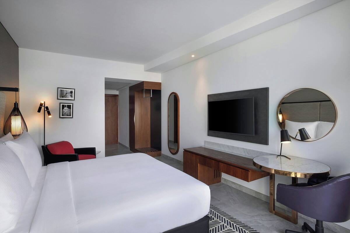 A modern hotel room with a large bed, a desk, a TV, and a mirror.