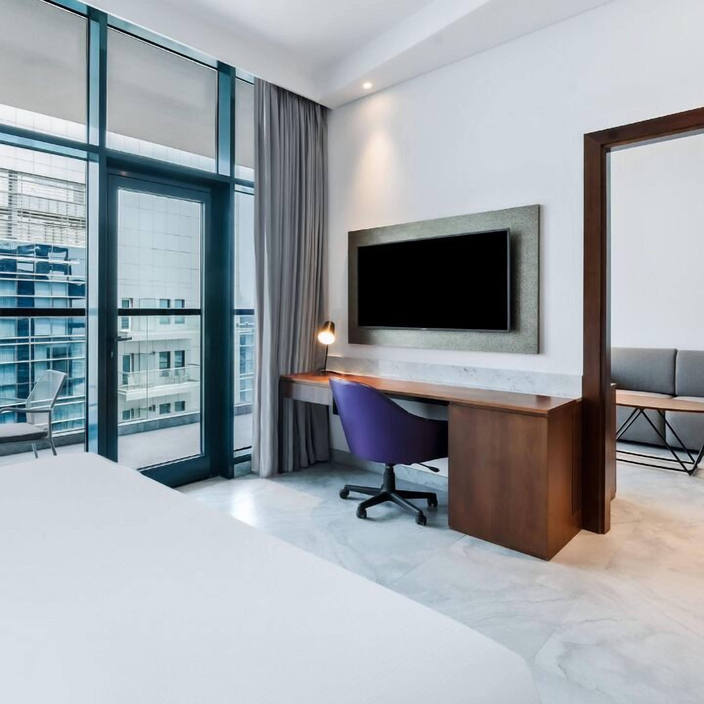Een moderne hotelkamer met een groot raam, een bureau met stoel, een flatscreen televisie aan de muur en een bank.
