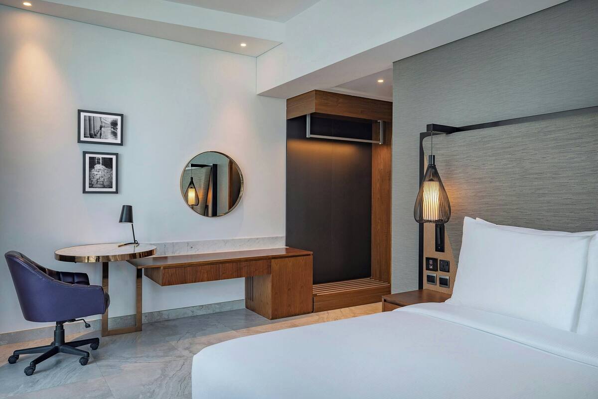 A modern hotel room with a bed, desk, chair, and a large mirror.