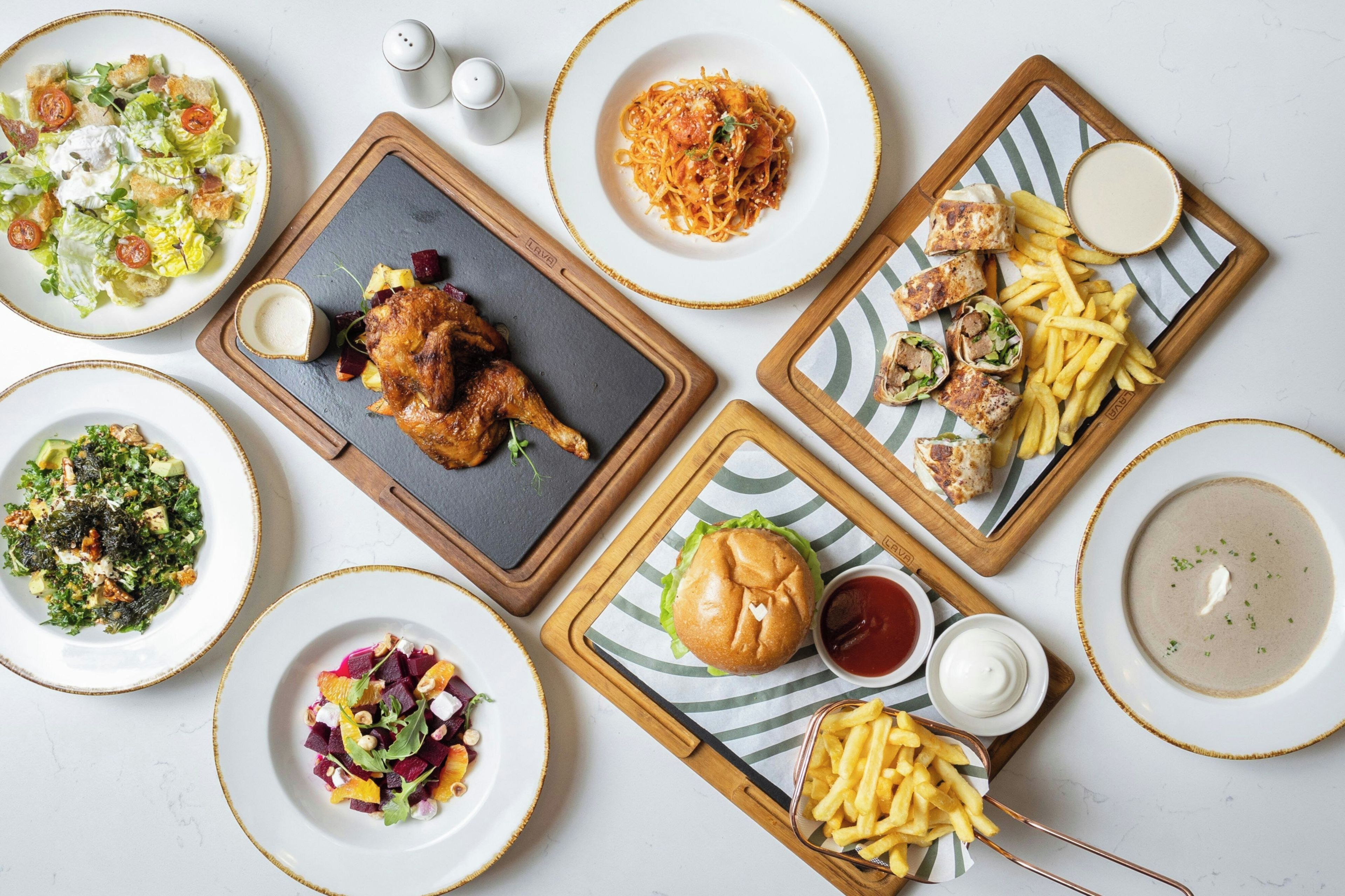 A variety of dishes including a salad, pasta, chicken, burger, fries, and soup, arranged on a table.