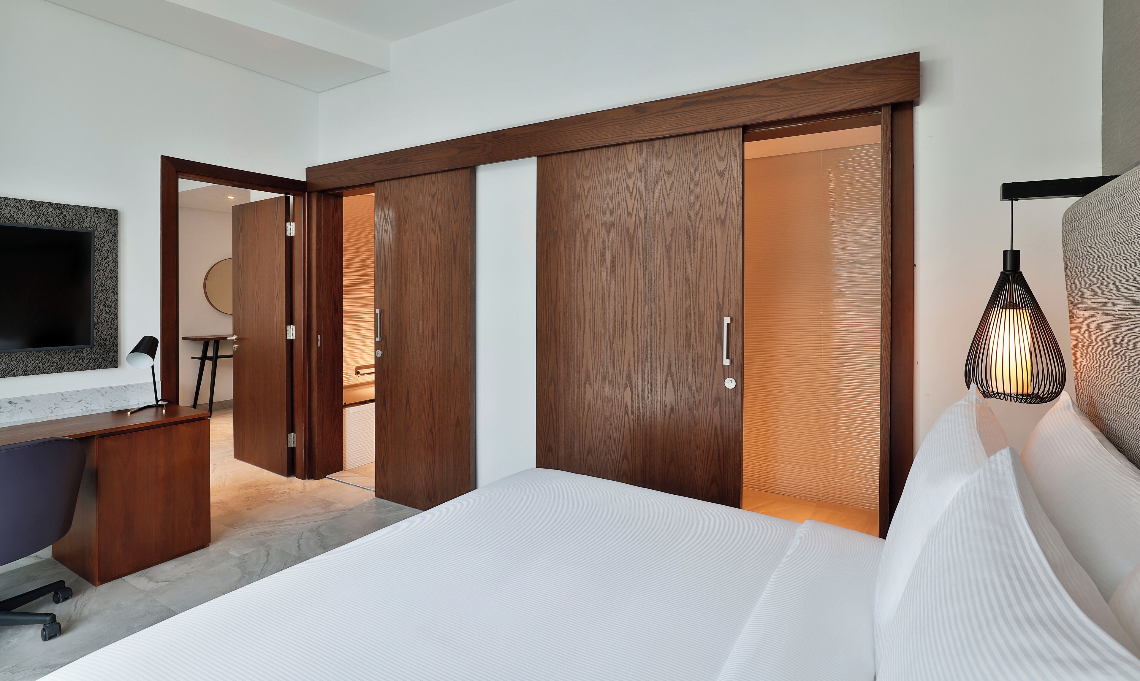 A modern bedroom with a large bed, wooden wardrobe, and a desk with a TV.