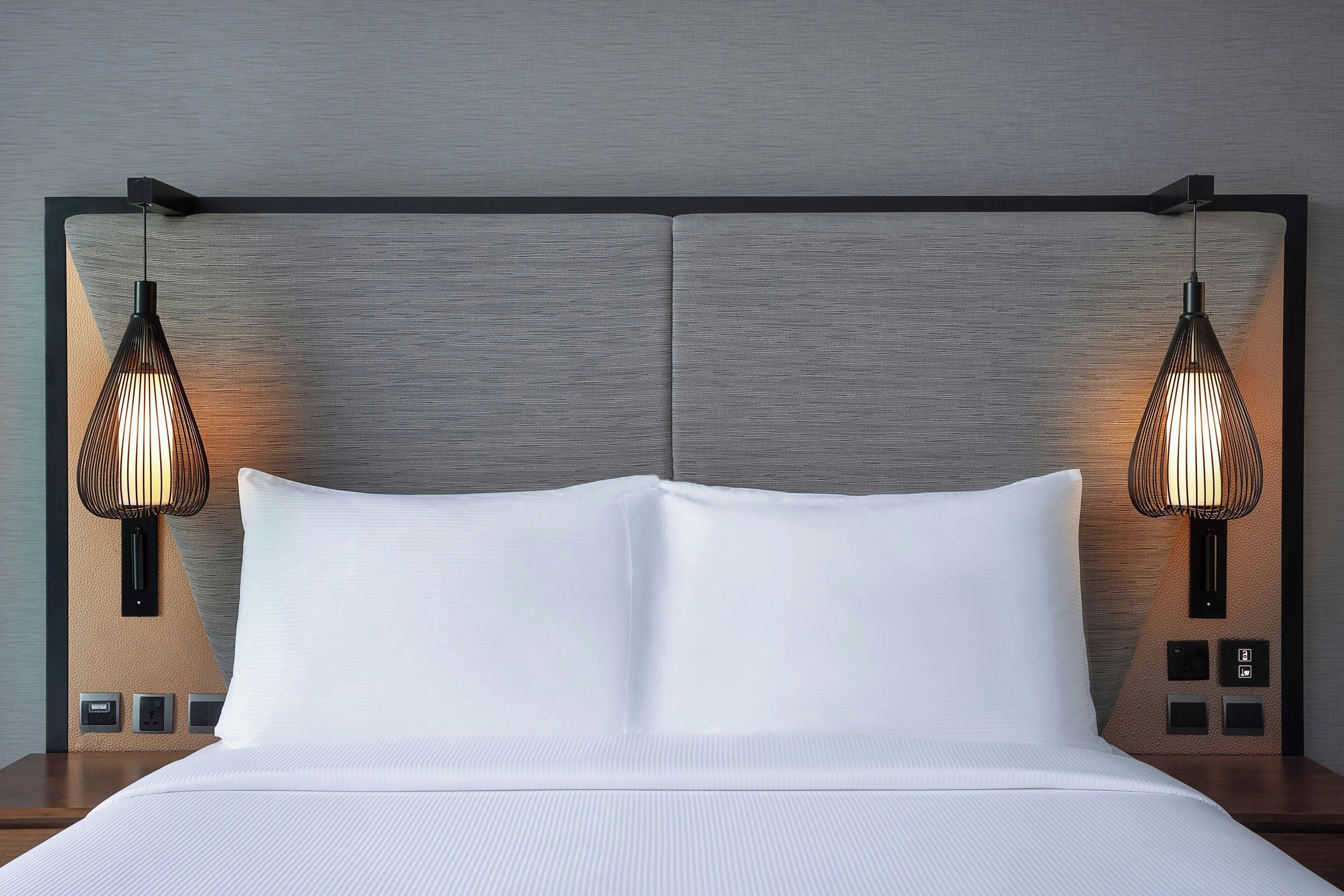 A neatly made bed with a headboard, two wall-mounted lamps, and a nightstand with a power outlet.