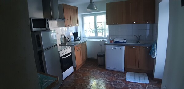 Cocina compacta con microondas, estufa y lavavajillas. Hay una ventana que ofrece luz natural y vistas a la vegetación.