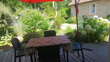 En udendørs terrasse med et bord og stole, omgivet af frodigt grønt og en stengård.