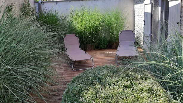 A wooden deck with two lounge chairs, surrounded by tall grasses and shrubs.
