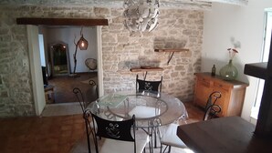 A rustic dining area with a round glass table, black chairs, and a stone wall backdrop.