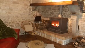 A stone fireplace with a fire, a red sofa, a wicker chair, and a table with a glass top.