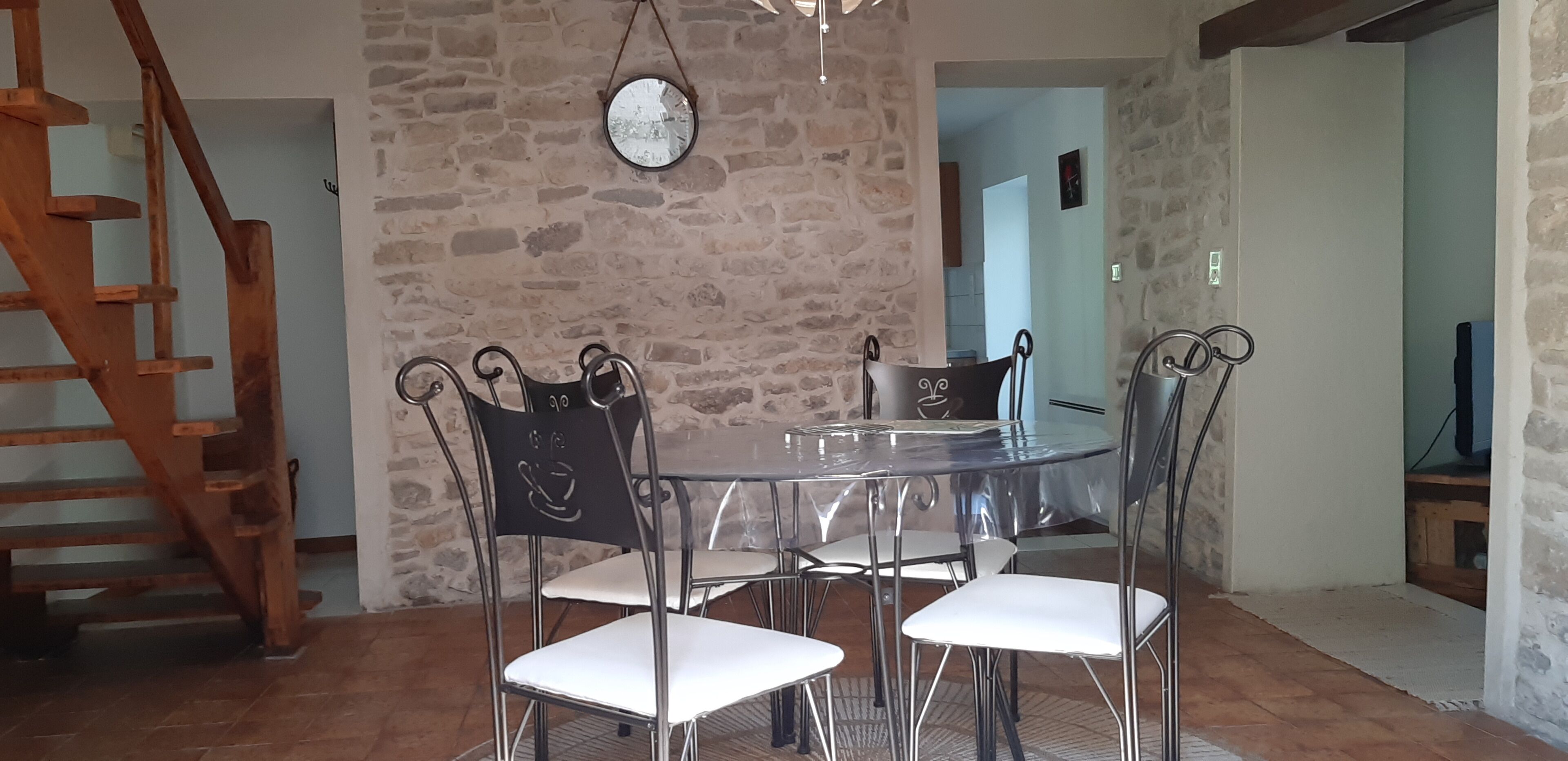 A dining area with a round glass table and metal chairs, a wooden staircase, and a stone wall.