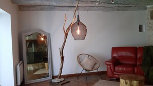 A living room with a red leather sofa, a wicker chair, a hanging light fixture, and a stone fireplace.
