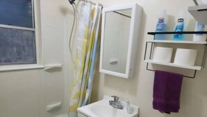 Une salle de bain équipée d’une baignoire, d’un lavabo, de toilettes, d’un miroir et d’étagères contenant des articles de toilette.