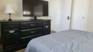 Une chambre à coucher avec un lit, une commode, un téléviseur et deux portes blanches.
