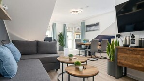 A modern living room with a sofa, two round tables, a TV, and a desk with a computer.