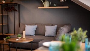 A modern living room with a sofa, a coffee table, and a small side table. There is a shelf with decorative items and a hanging plant.
