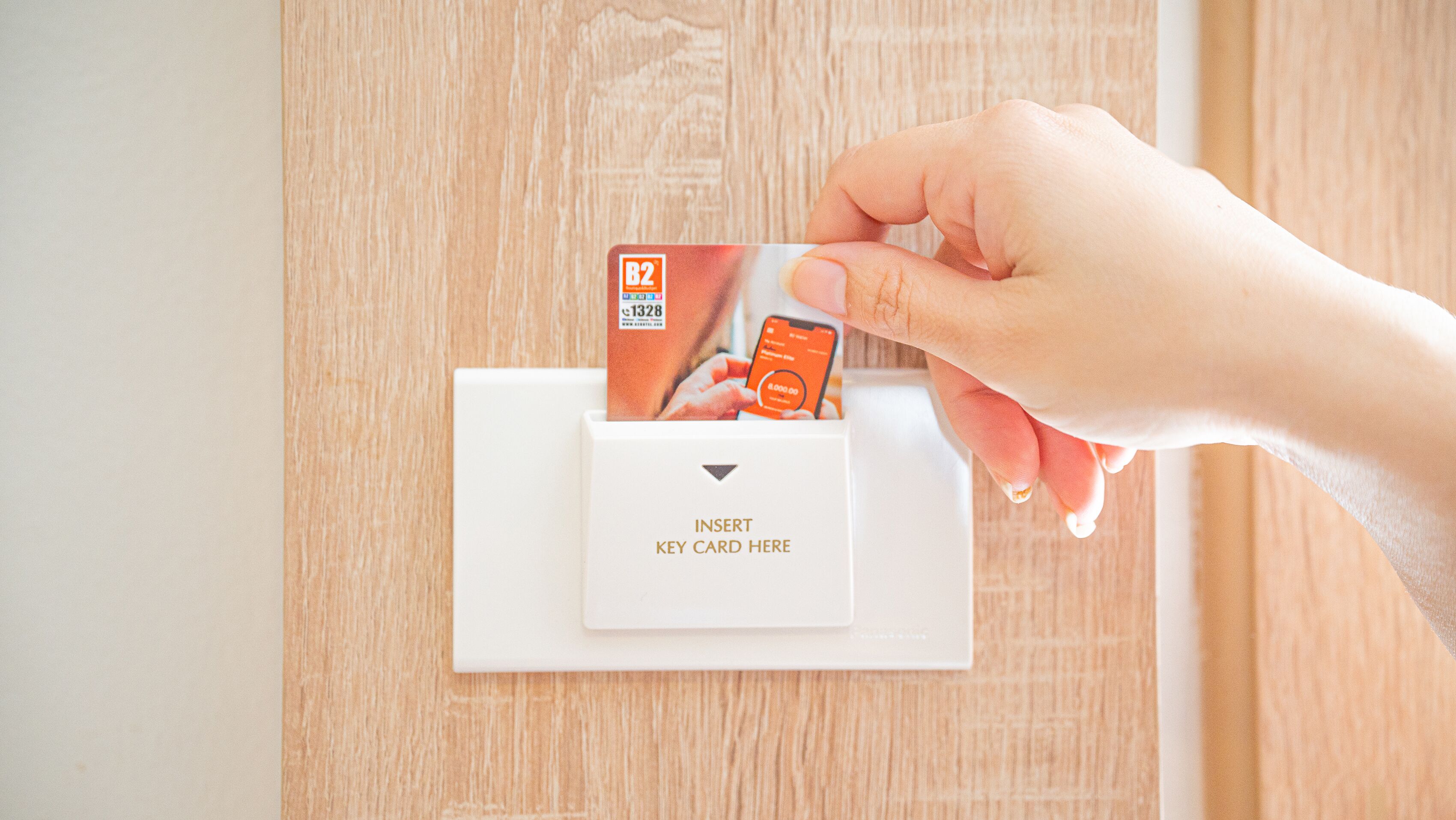 A hand inserting a key card into a card reader on a white panel.