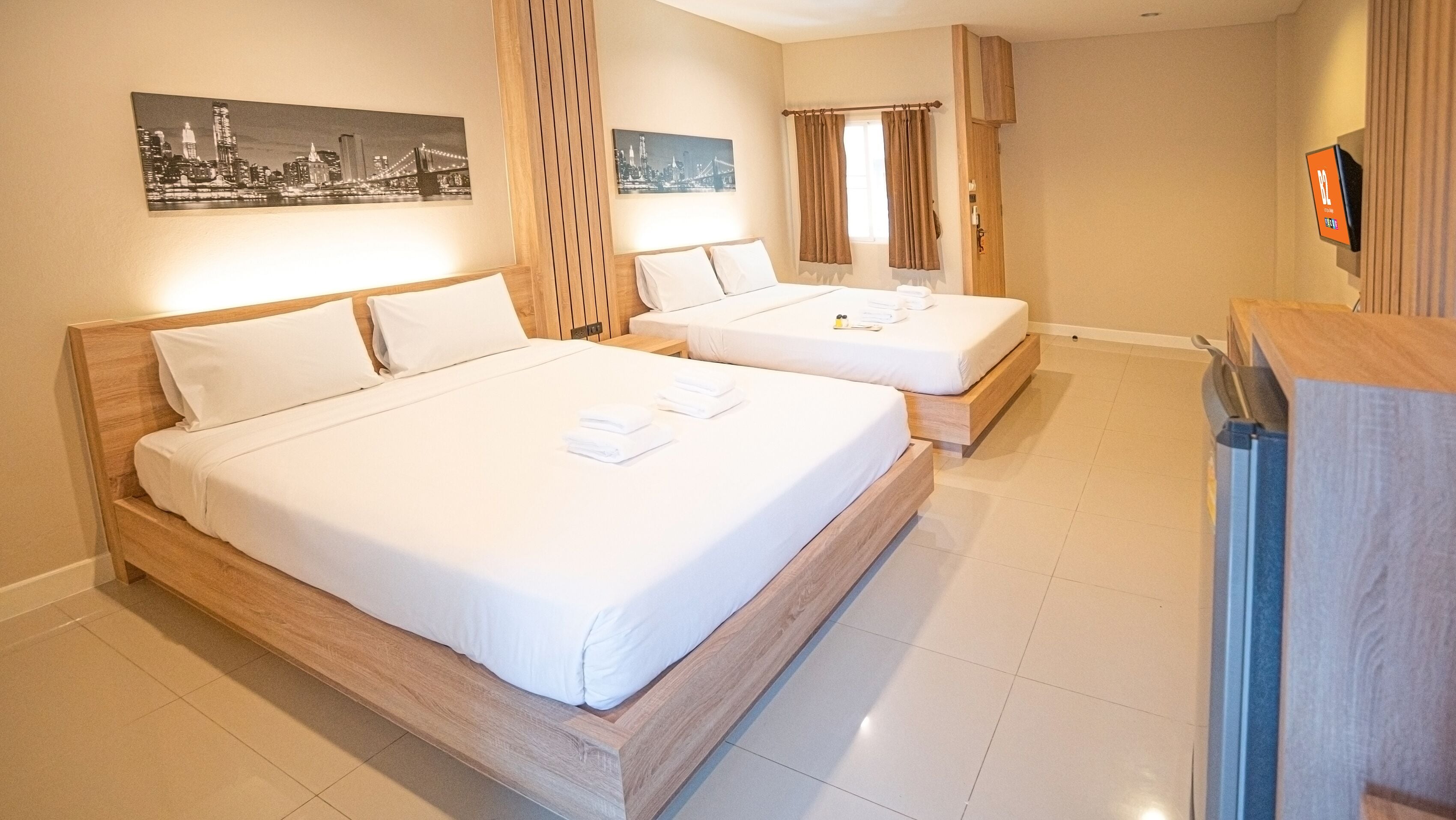 A hotel room with two wooden beds, white linens, and a flat-screen TV on the wall.