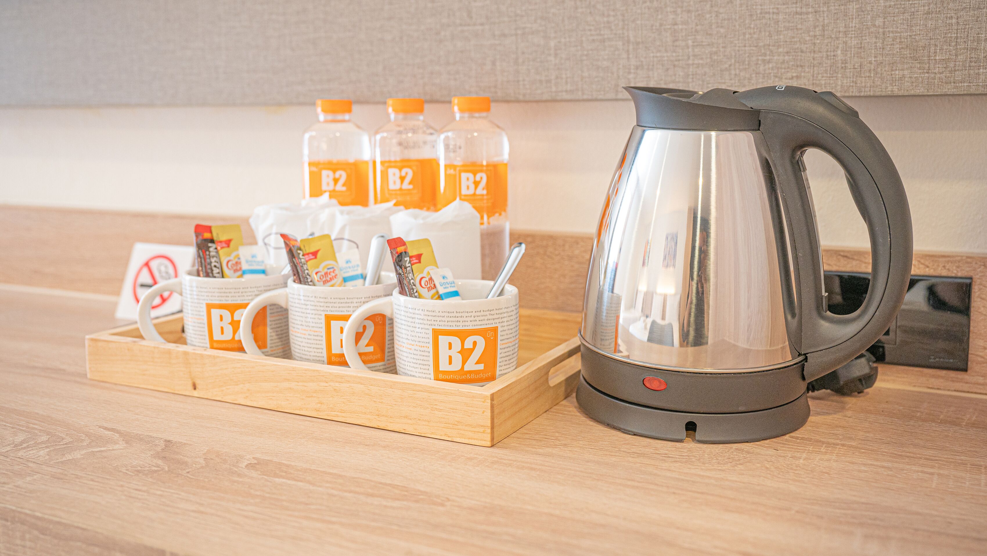 A kitchenette setup with a coffee maker, mugs, and coffee packets on a wooden tray.