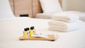Una cama bien hecha con toallas blancas dobladas y una bandeja con tres botellas de gel de ducha B2 y una pastilla de jabón.