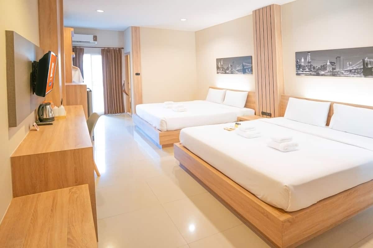 A hotel room with two beds, a wooden desk, a flat-screen TV, and cityscape artwork on the walls.