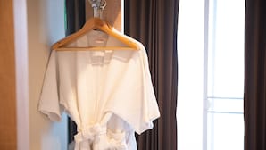Una bata blanca colgada de una percha de madera en una habitación con ventana y cortinas.
