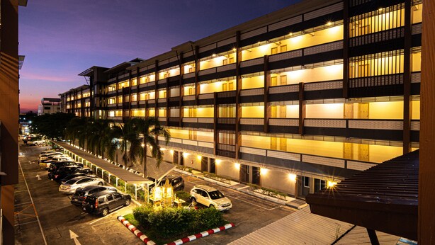 Un hotel de varios pisos con una fila de coches estacionados al frente, una entrada bien iluminada y una vista clara de la fachada del edificio.
