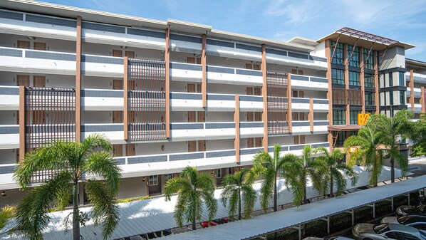 Un hôtel à plusieurs étages doté de balcons, d’un parking couvert et de palmiers.