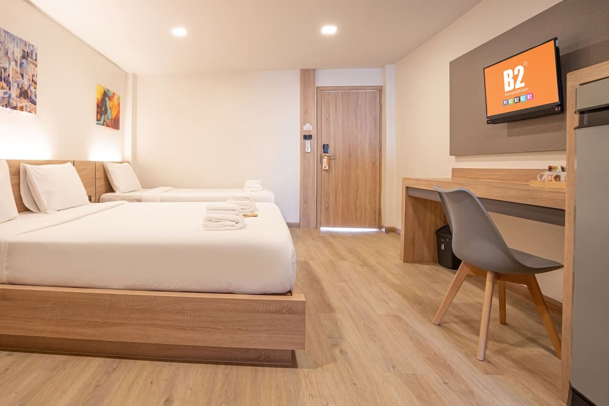 A hotel room with two beds, a desk, a chair, and a TV displaying 'B2 Boutique & Budget'.
