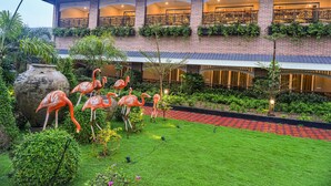 A hotel with a brick facade, multiple balconies with intricate railings, and a well-maintained garden with flamingo statues. - Mayfair Oasis Resort & Convention (Jharsuguda)