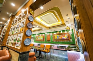 Un interior de restaurante con una zona de comedor central, diversas opciones de asientos y un techo decorativo.