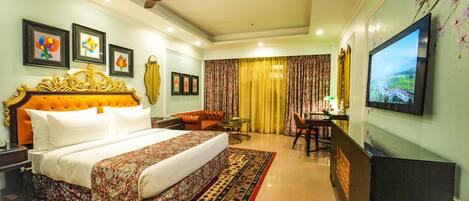 A hotel room with a large bed, a desk, a chair, a television, and a ceiling fan.