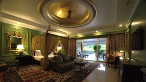 A spacious room with a large bed, a sitting area with a sofa and armchairs, a coffee table, and a view of the outdoors through a sliding glass door. - Mayfair Oasis Resort & Convention (Jharsuguda)