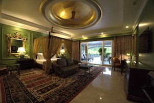 Una habitación amplia con una cama grande, una sala de estar con sofá y sillones, una mesa de centro y vistas al exterior a través de una puerta corrediza de vidrio.