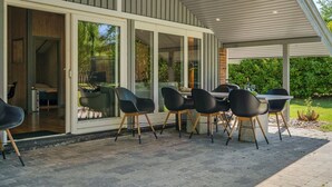 Une terrasse extérieure moderne, dotée d’une table et de chaises, de grandes portes-fenêtres coulissantes donnant sur un espace abrité et d’un chemin en briques.