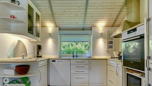 Une cuisine moderne avec des meubles blancs, un lave-vaisselle intégré, un four double et une fenêtre donnant sur un espace verdoyant.
