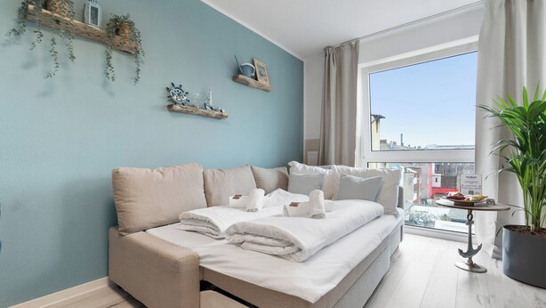 A modern bedroom with a sofa bed, a large window with a city view, and decorative shelves on the wall. - Superior 2-zimmer 36qm Kingsize Boxspring 55' TV Home-office 11min Hbf (Duisburg)