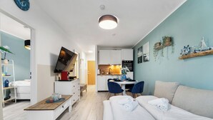 A modern hotel room with a wooden bench, a white sofa, and a dining area with a table and chairs. - Superior 2-zimmer 36qm Kingsize Boxspring 55' TV Home-office 11min Hbf (Duisburg)