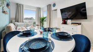A dining area with round tables, blue plates, and glasses. There is a sofa and a TV in the background. - Superior 2-zimmer 36qm Kingsize Boxspring 55' TV Home-office 11min Hbf (Duisburg)