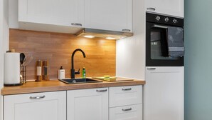 A modern kitchen with white cabinets, a wooden countertop, a stainless steel sink, and a black oven. - Superior 2-zimmer 36qm Kingsize Boxspring 55' TV Home-office 11min Hbf (Duisburg)