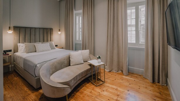 Une chambre à coucher moderne avec un grand lit, un canapé incurvé, une petite table d’appoint et une grande fenêtre avec des rideaux.