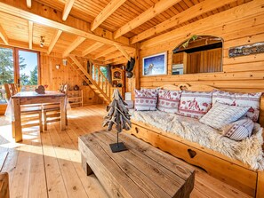 Een houten cabin interieur met een eethoek, een bank met opvallende kussens en een trap naar een hoger niveau.