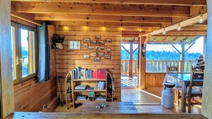 L’intérieur d’un chalet en bois, avec une bibliothèque, une table et une vue sur l’extérieur.